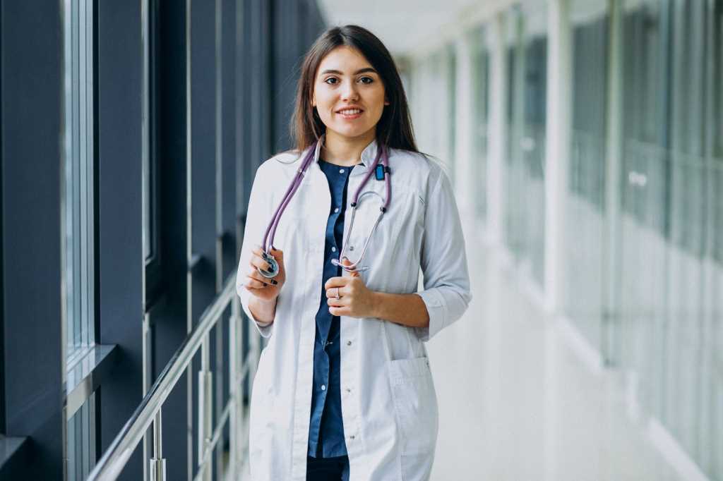 A lady standing around a glass wall wearing a doctor coat