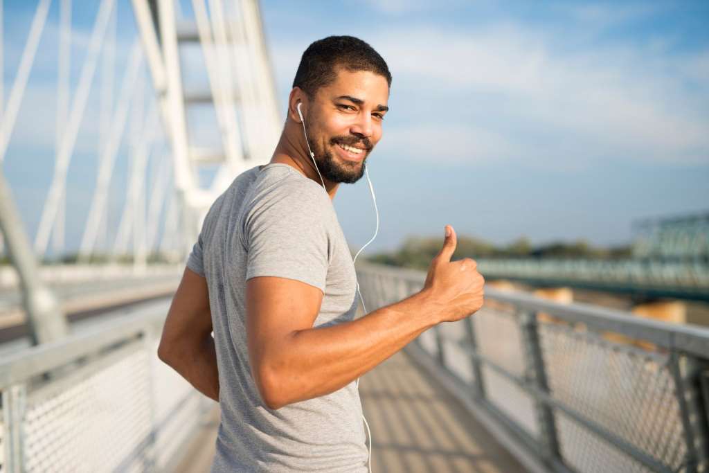 smiling athlete with earphones holding thumbs up ready for training