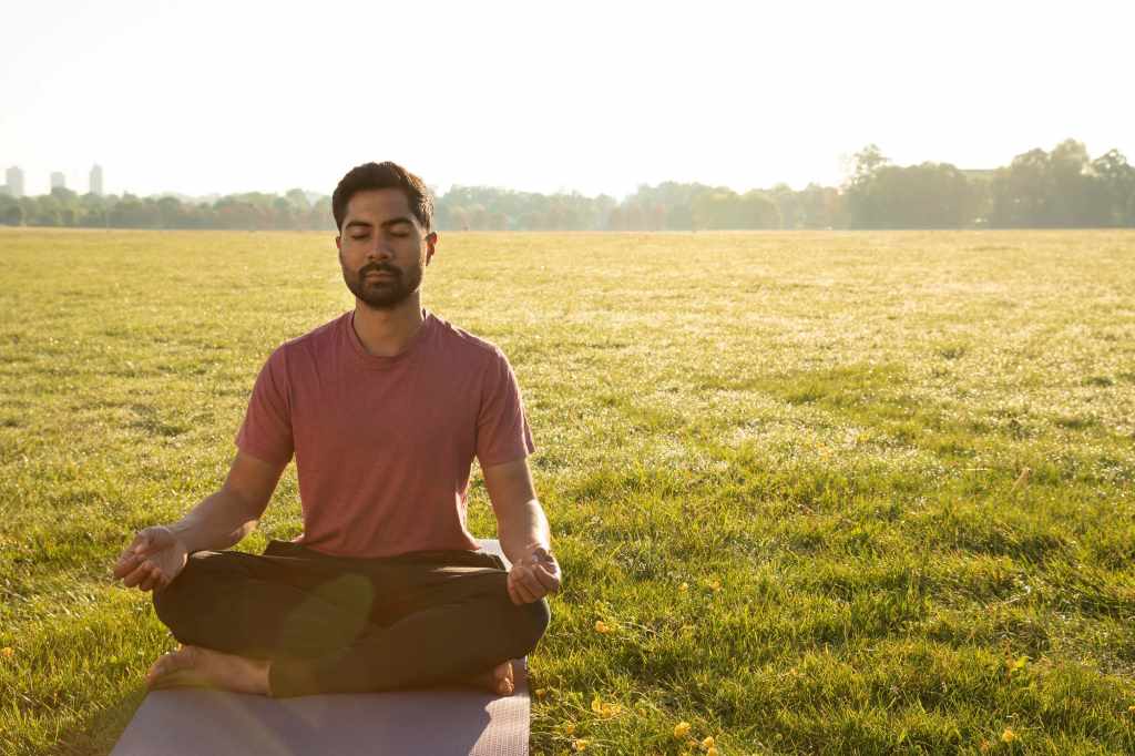 man meditating outdoors on yoga mat